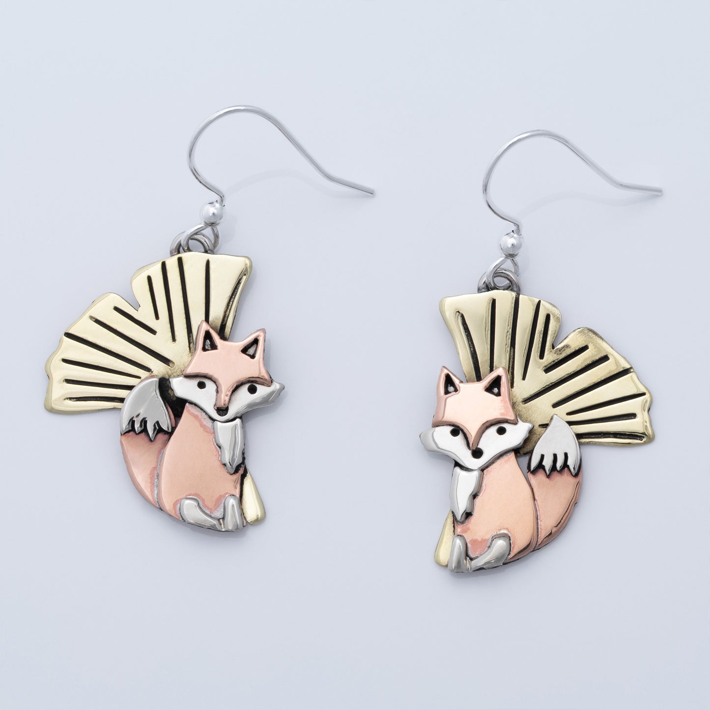 Pair of fox-themed earrings with brass, copper, and silver accents on a light gray background