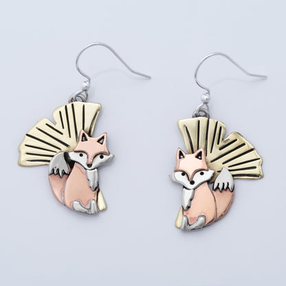 Pair of fox-themed earrings with brass, copper, and silver accents on a light gray background