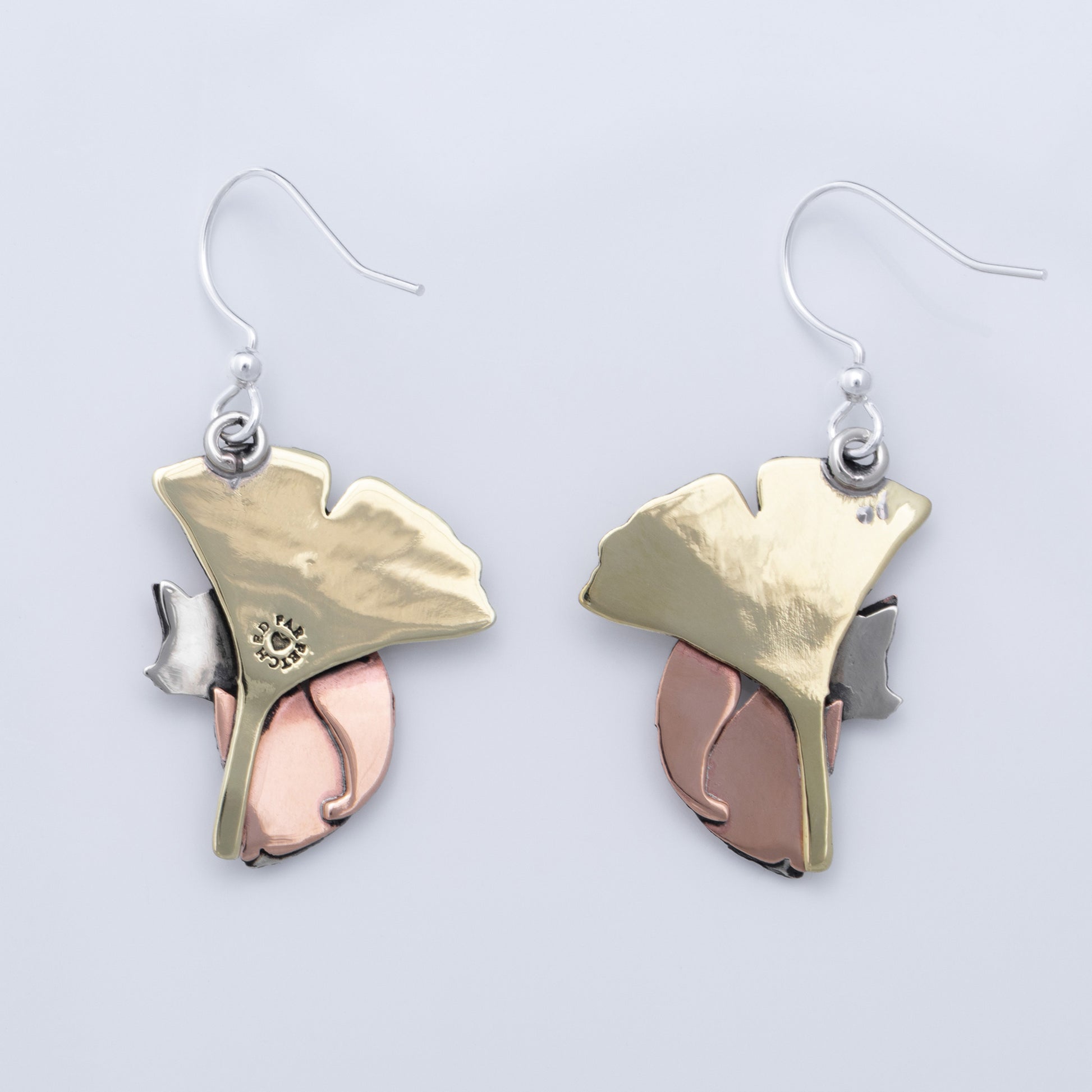The back of a pair of fox and leaf earrings with brass, silver, and copper design on a light gray background
