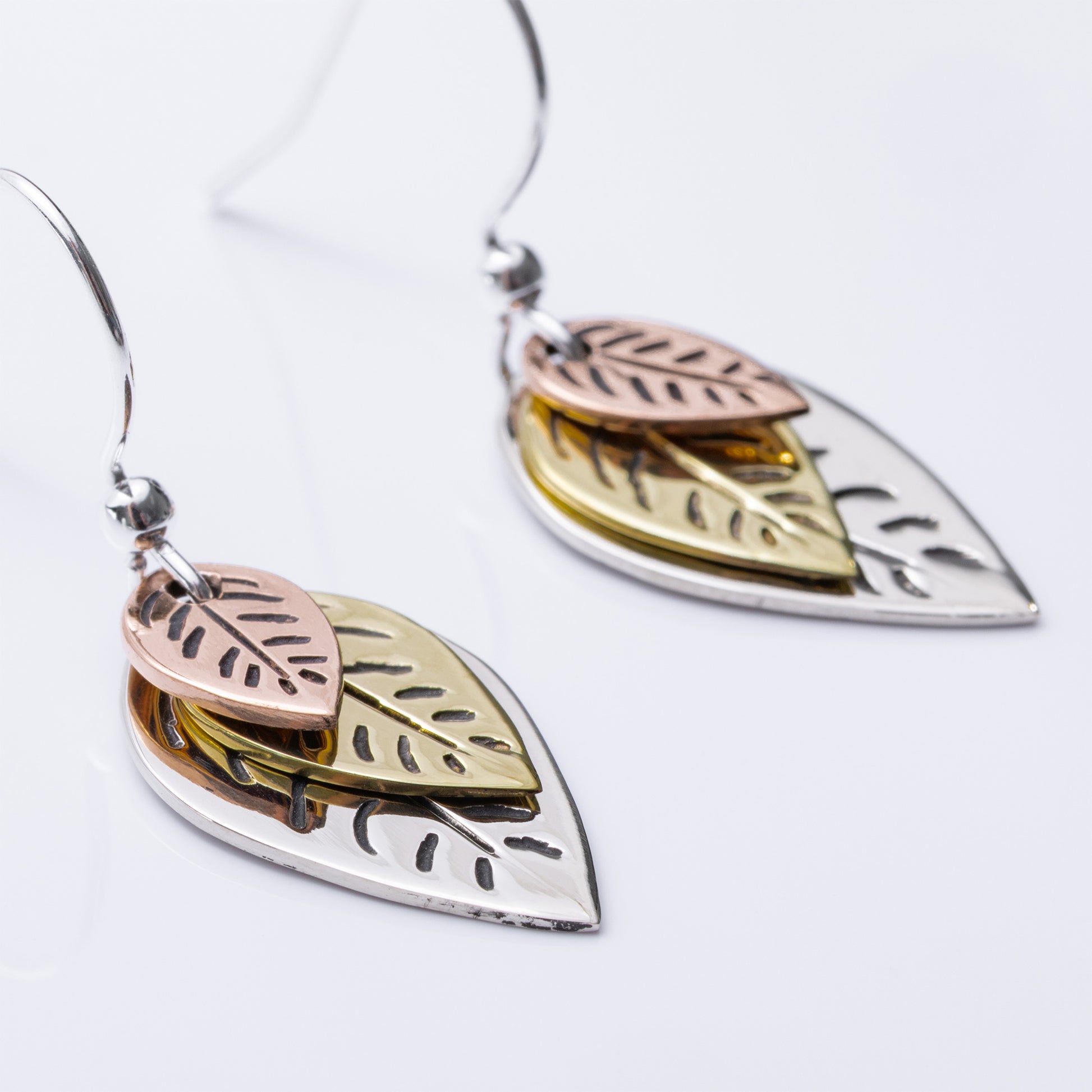 Leaf-shaped earrings in silver, gold, and rose gold on a white background