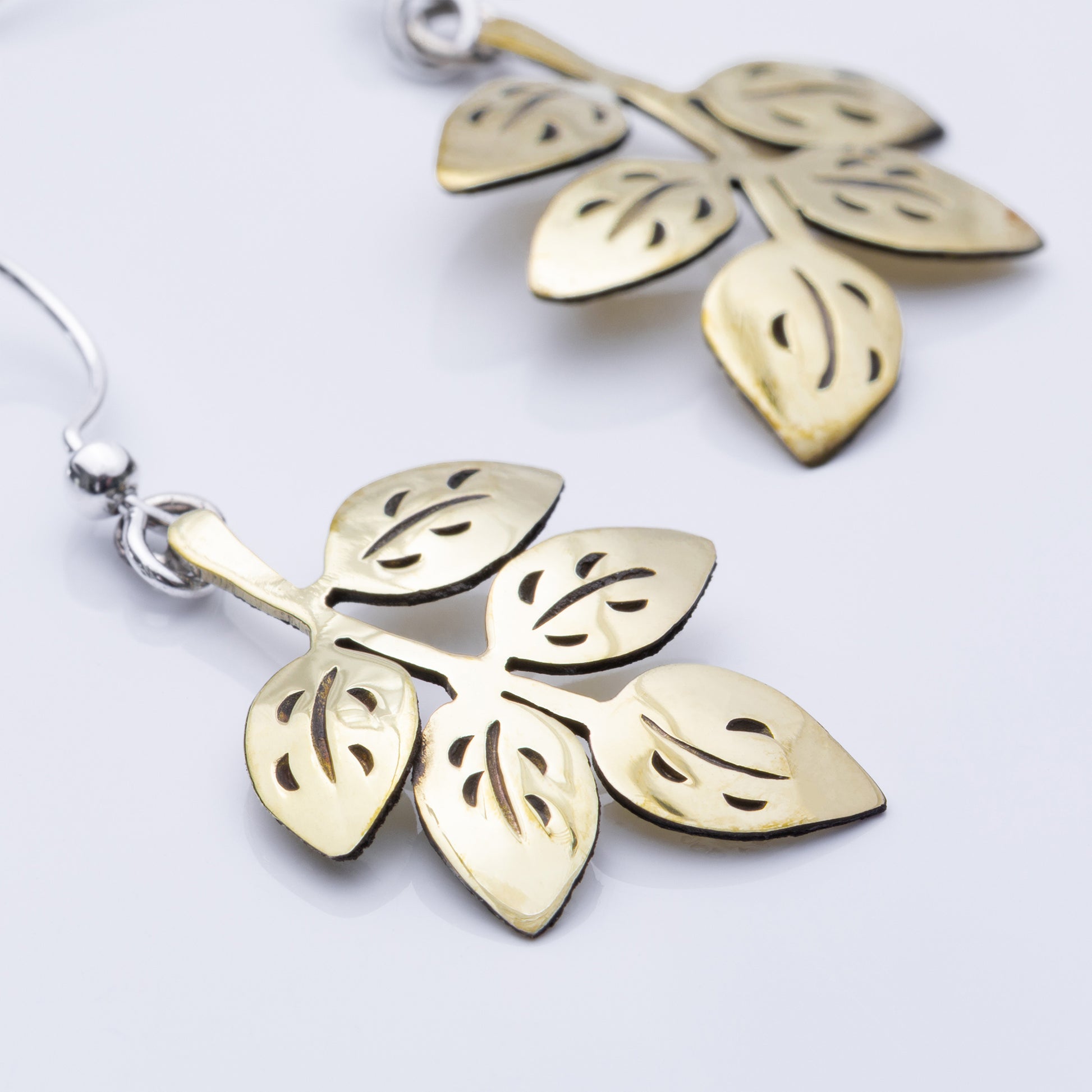 Close up of brass leaf-shaped earrings on a white background