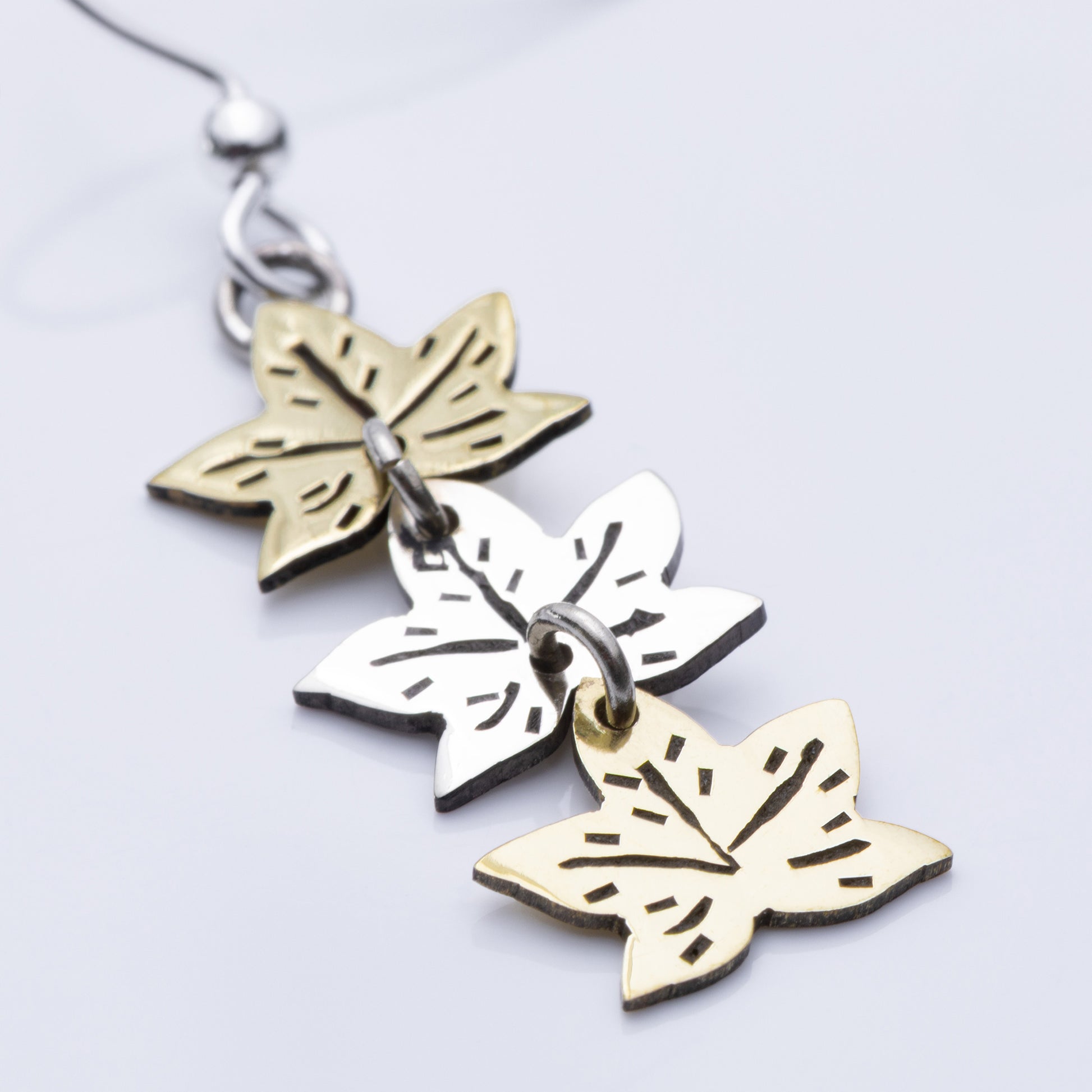 Pair of leaf-shaped earrings in gold and silver tones on a light gray background