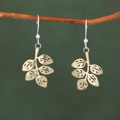 Gold leaf earrings hanging from a branch against a green background