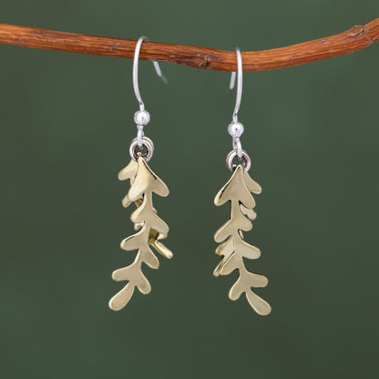 Brass leaf-shaped earrings hanging from a branch against a green background