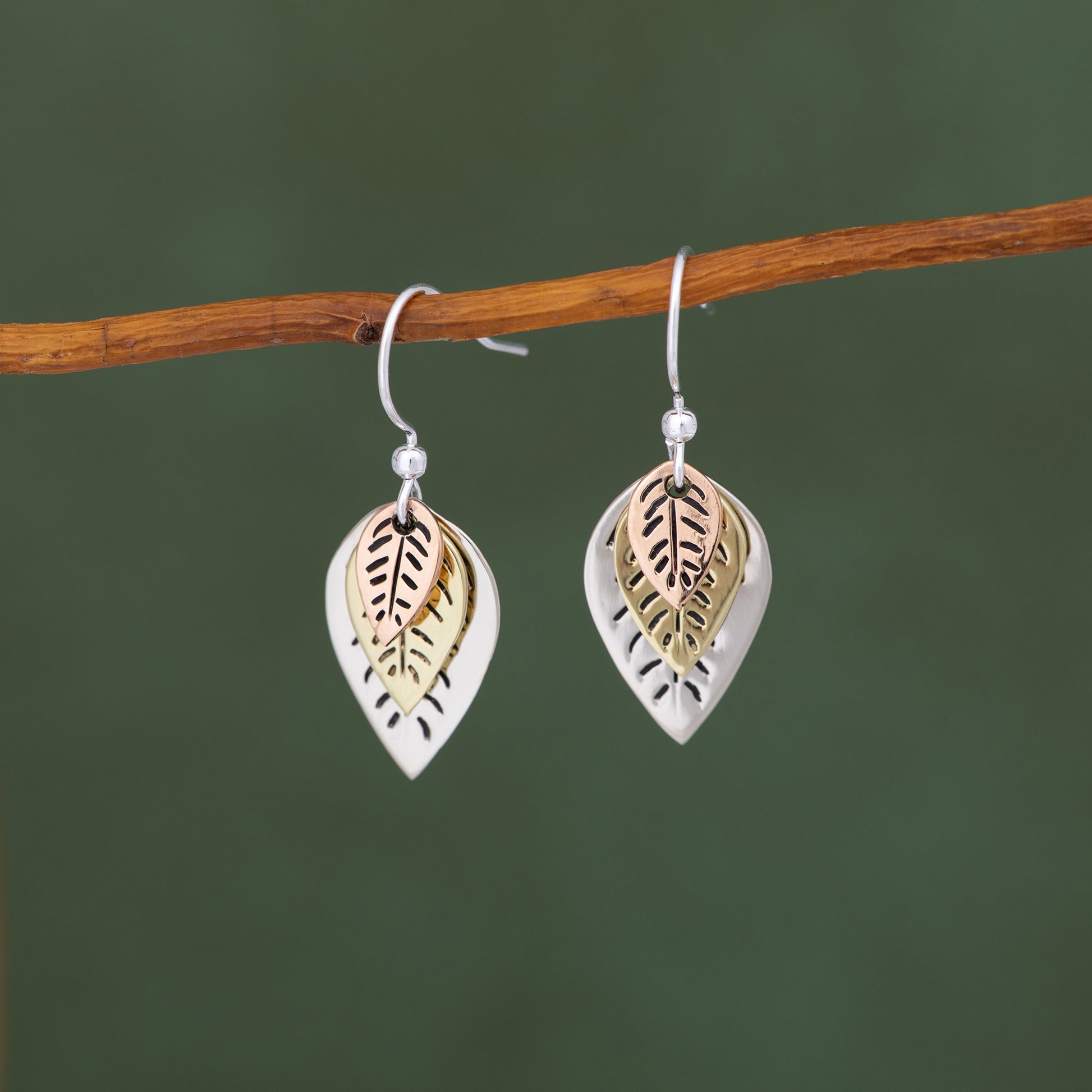 Pair of leaf-shaped earrings on a branch with a green background