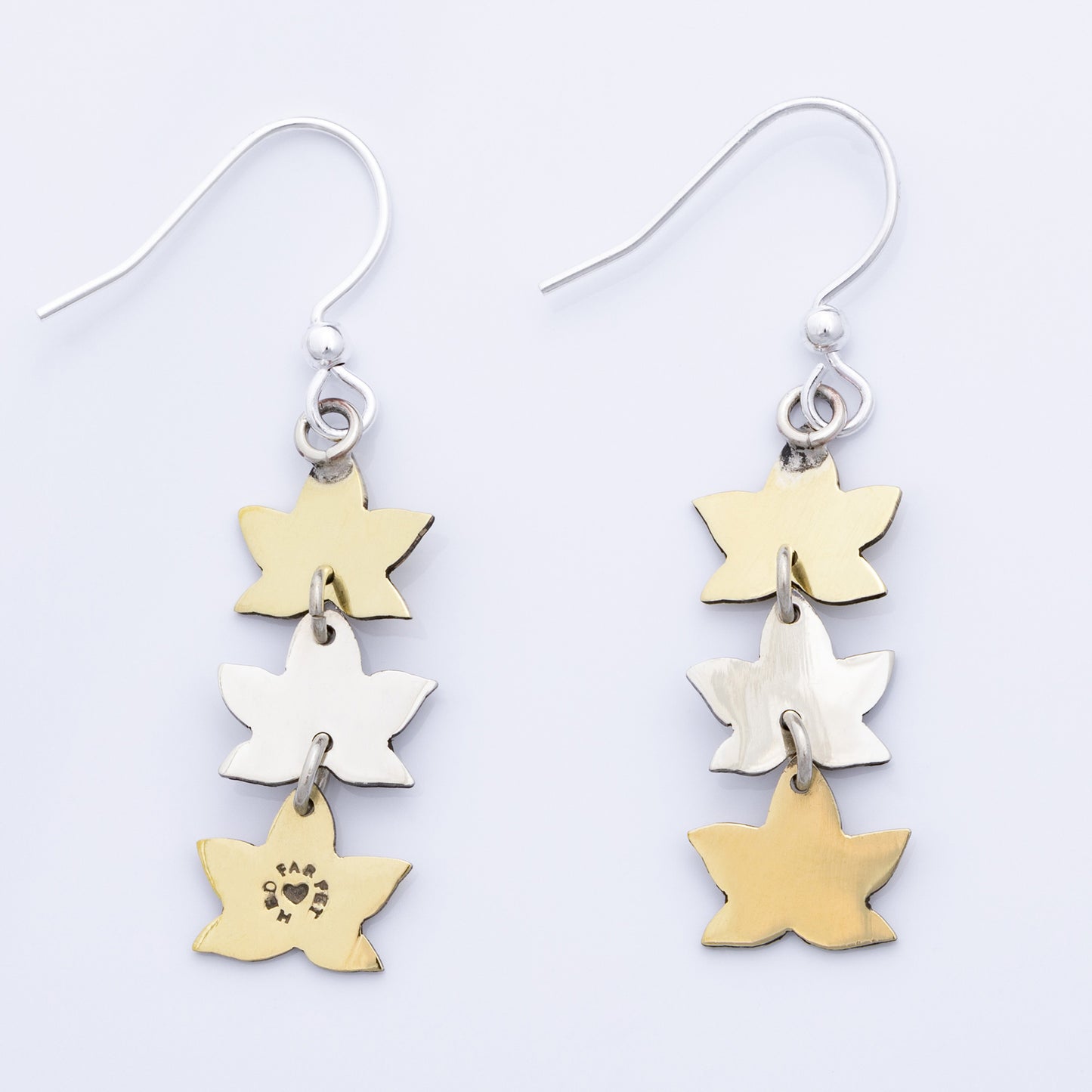 Backs of leaf-shaped earrings in gold and silver on a light gray background