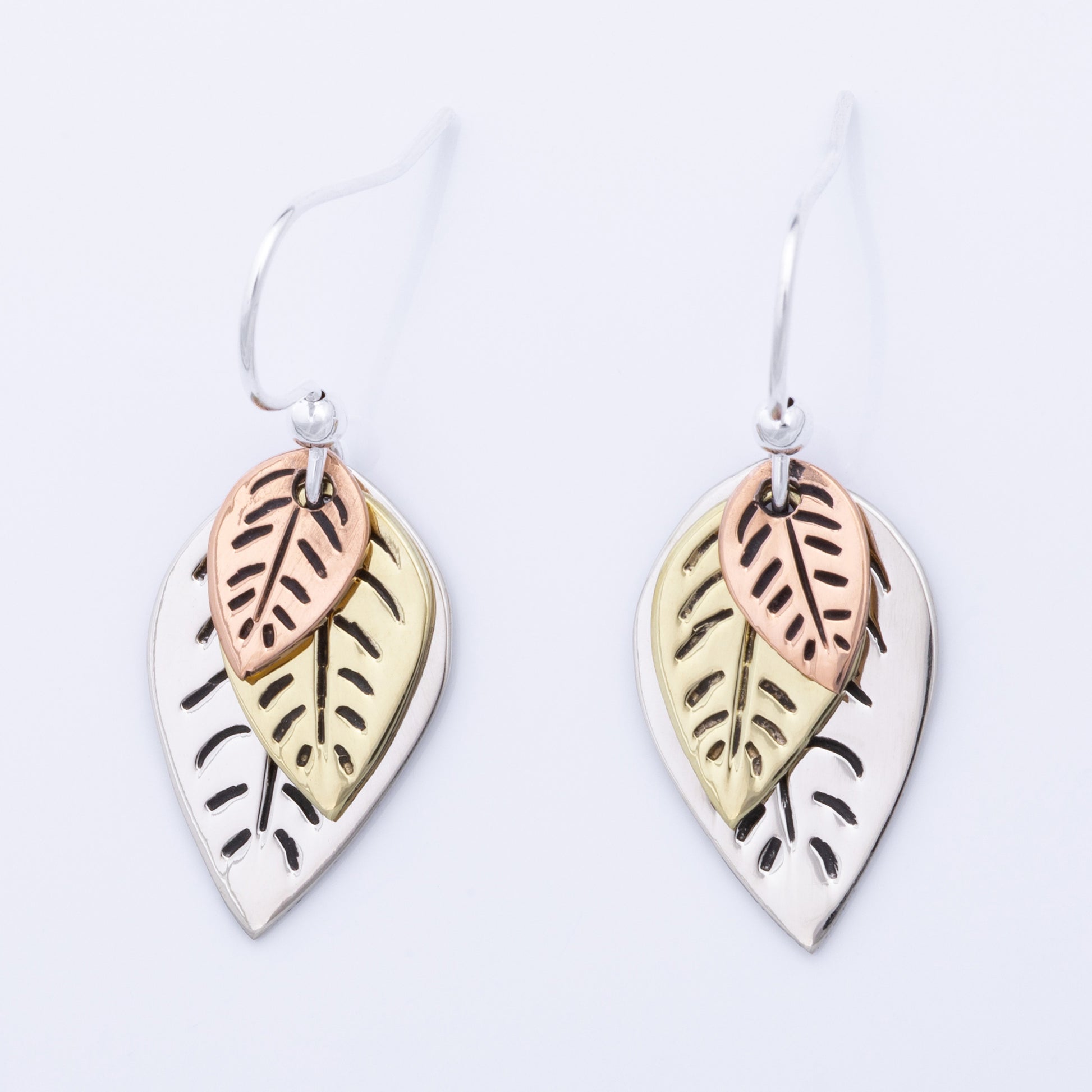 Pair of leaf-shaped earrings with copper, brass, and silver finishes on a light gray background.
