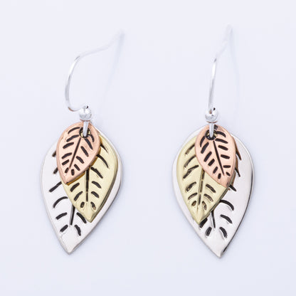 Pair of leaf-shaped earrings with copper, brass, and silver finishes on a light gray background.
