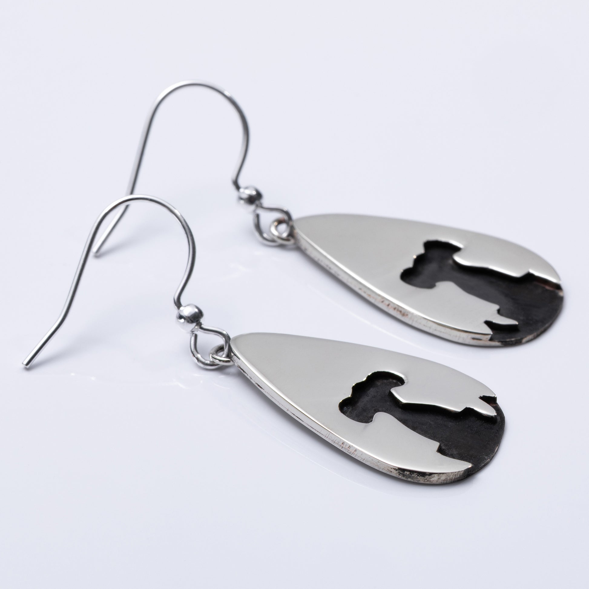 Close up of a pair of silver teardrop-shaped earrings with engraved designs on a light gray background
