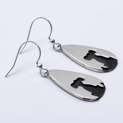 Close up of a pair of silver teardrop-shaped earrings with engraved designs on a light gray background