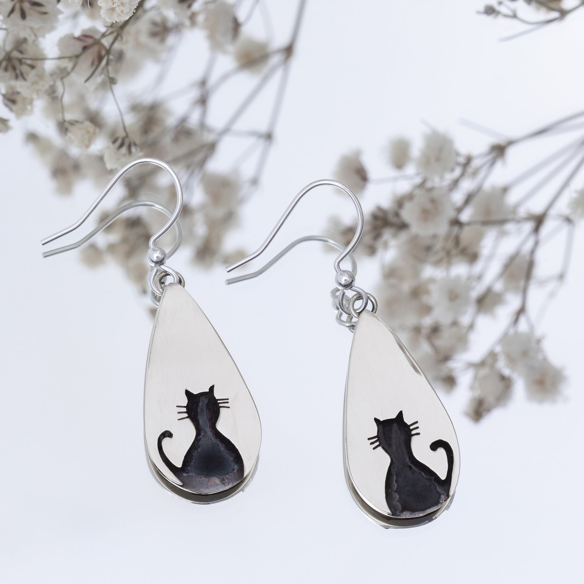 Teardrop-shaped earrings with black cat designs on a white background.