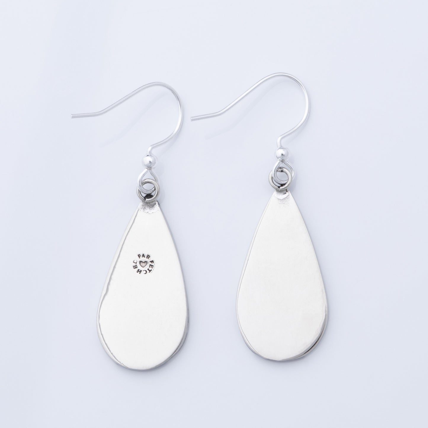 The back of silver teardrop earrings on a light gray background.