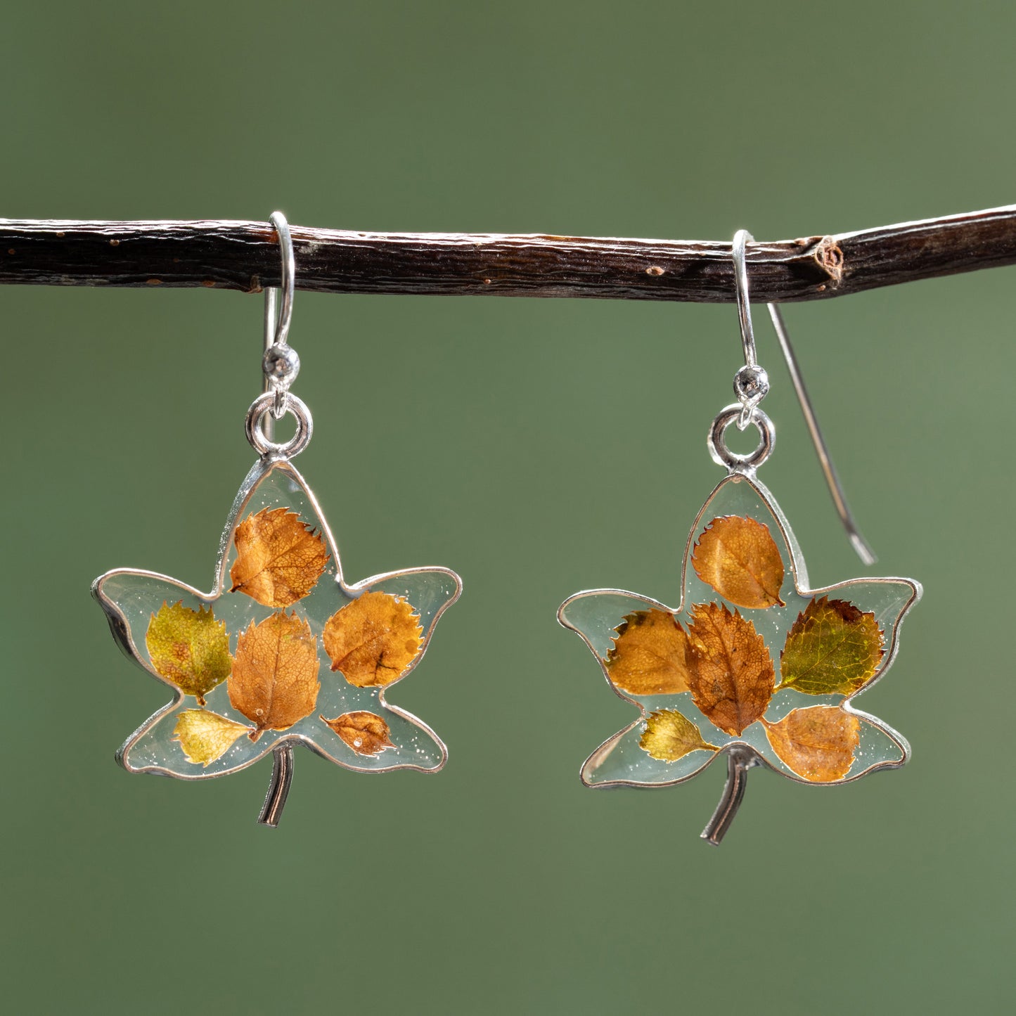 Maple leaf-shaped earrings with tiny leaves in resin on a branch against a green background