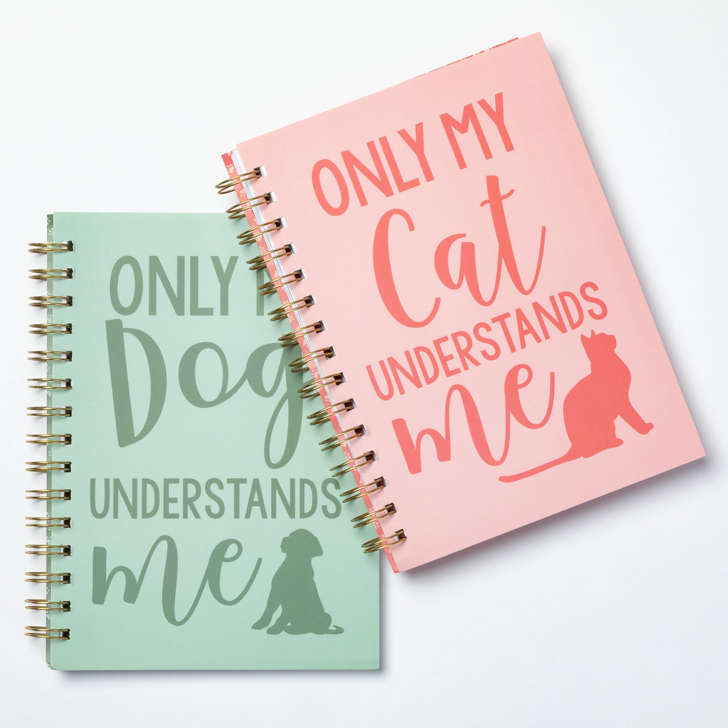 Two spiral-bound notebooks with humorous text designs on a light gray background.