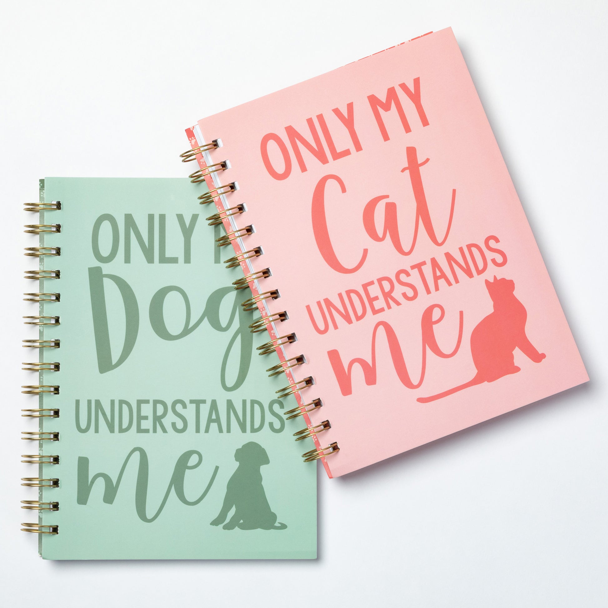 Two spiral-bound notebooks with humorous text designs on a light gray background.