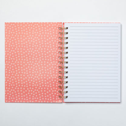 Open notebook with pink dotted cover and white lined pages on a light gray background