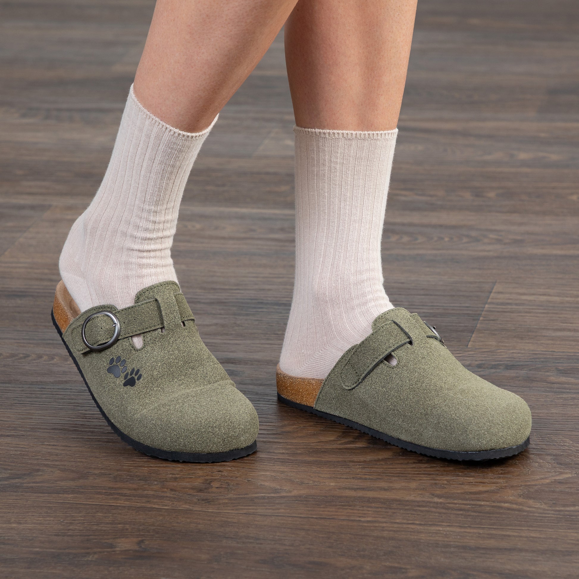 Person wearing green clogs with white socks on a wooden floor.