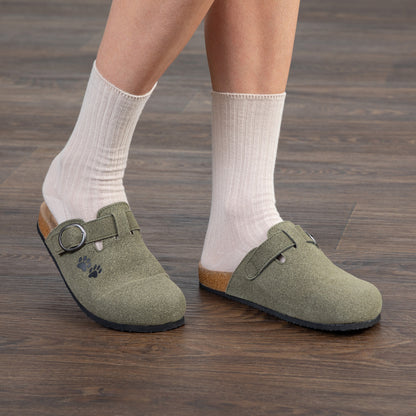 Person wearing green clogs with white socks on a wooden floor.