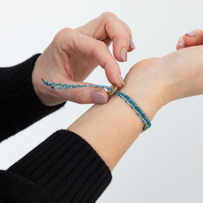 Person adjusting a blue braided bracelet on their wrist against a white background