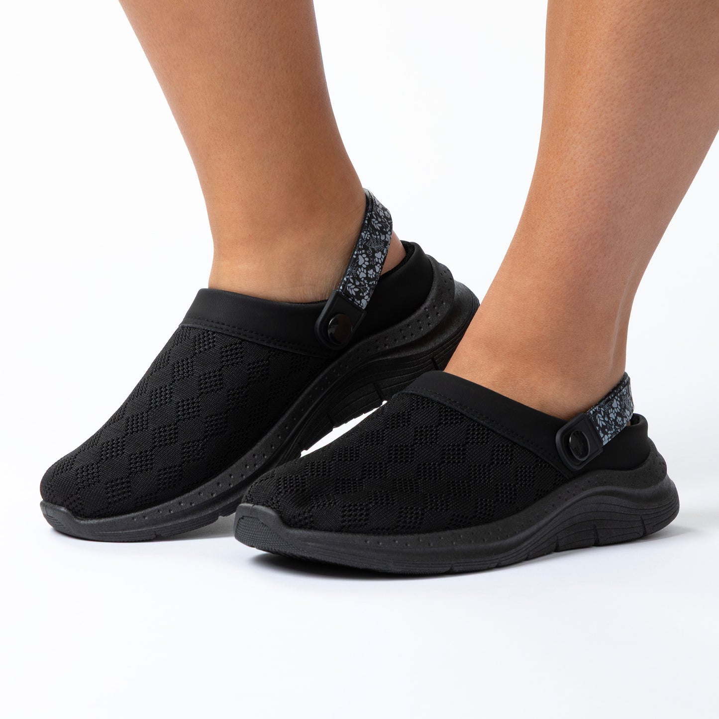 Black slip-on shoes worn by a person on a white background