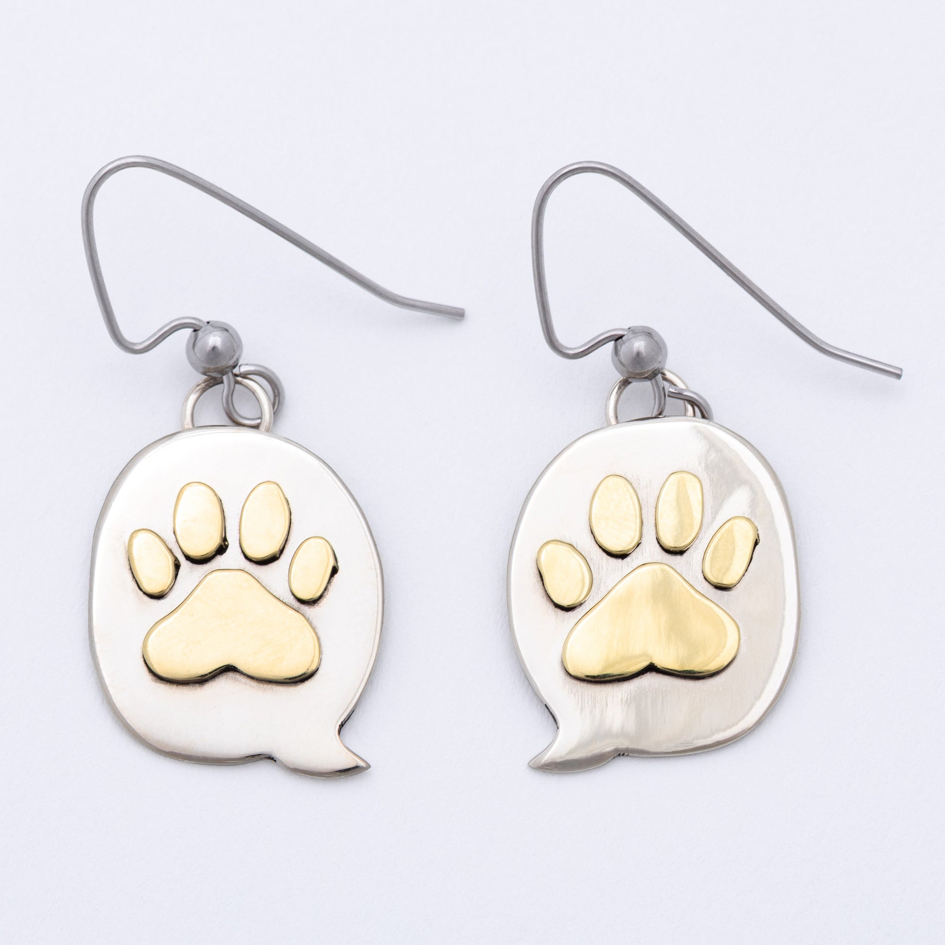 Paw print earrings with brass paw prints on silver speech bubble pendants against a white background