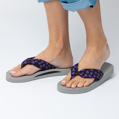 Gray flip-flops with purple floral straps worn by a person on a white background