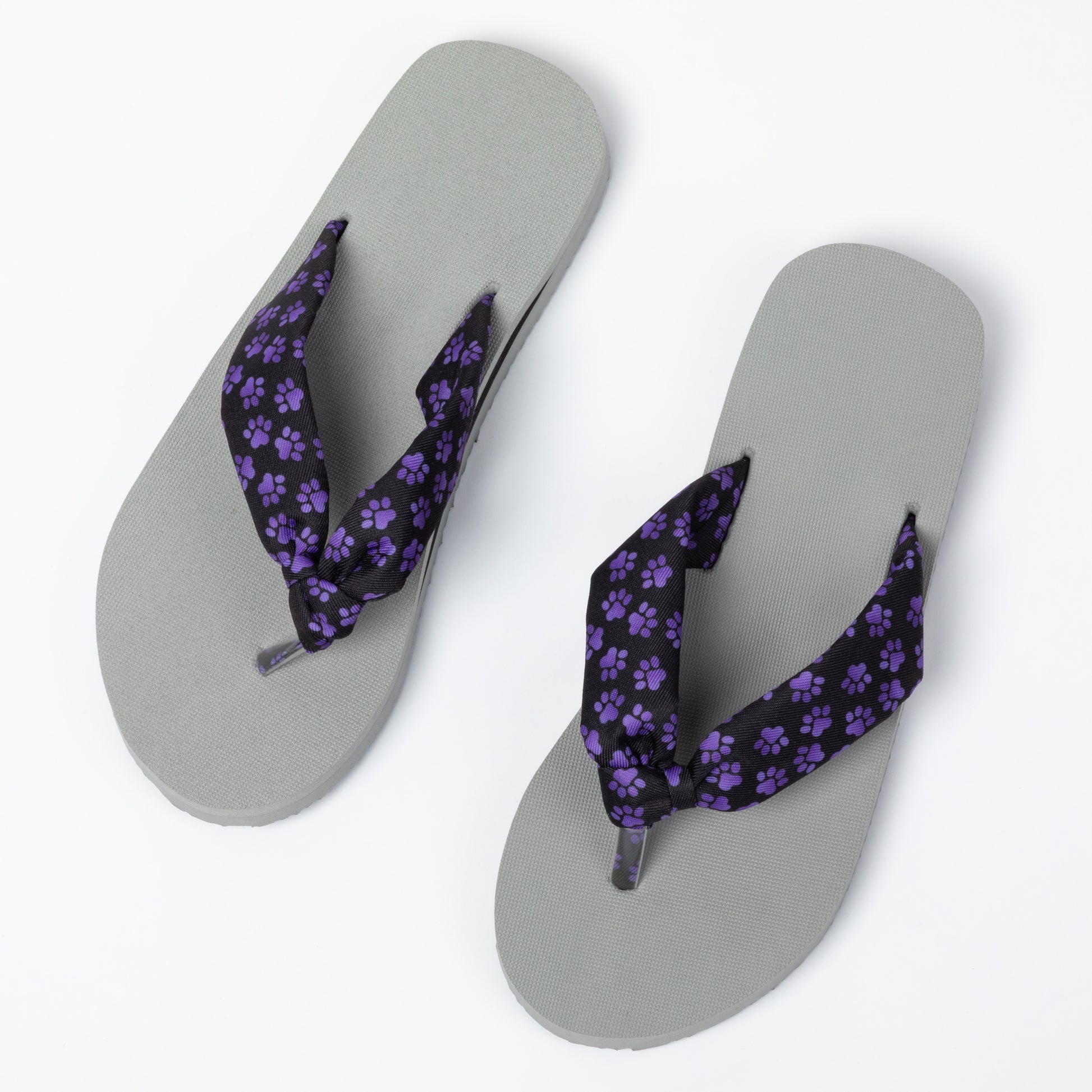 Gray flip-flops with purple paw print straps on a white background