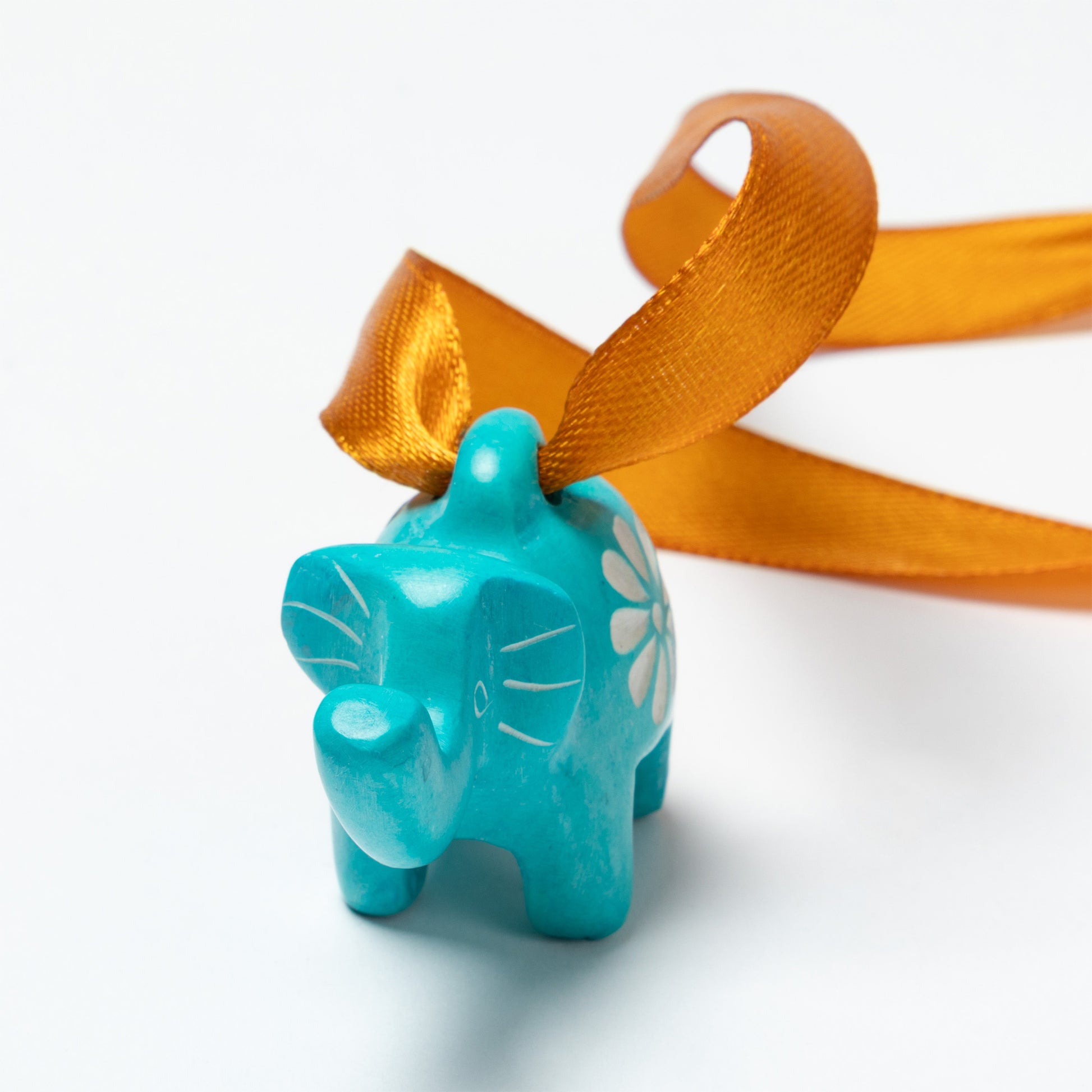 Turquoise elephant soapstone ornament with a white flower design on an orange ribbon against a white background