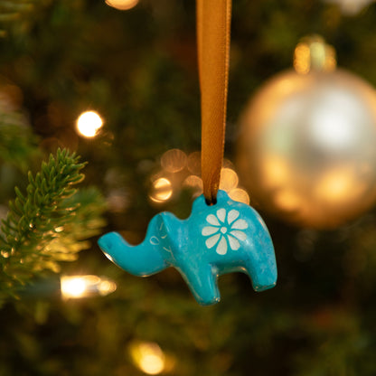 Blue elephant ornament with a white flower design hanging on a Christmas tree.