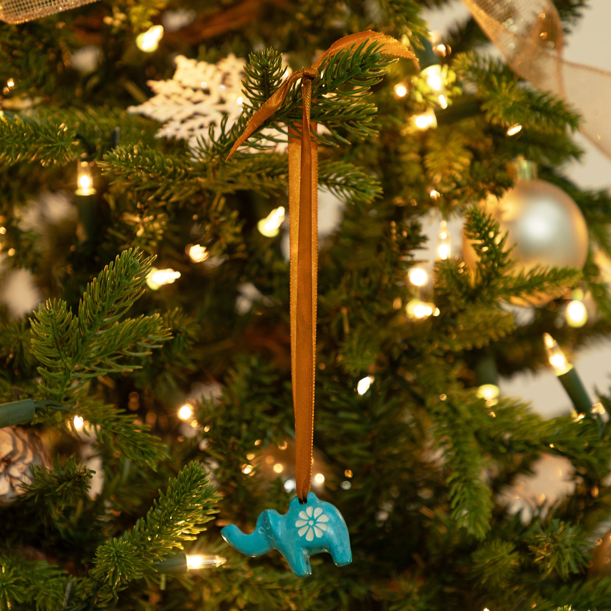 Blue elephant ornament hanging on a Christmas tree with lights and decorations.
