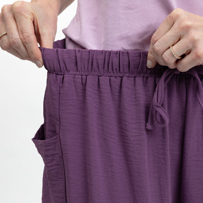 Purple pants with an elastic waistband being adjusted by hands on a white background