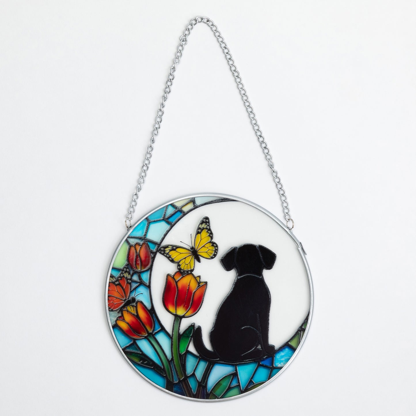 A circular stained-glass-style hanging ornament with a silver chain, featuring a black dog silhouette, a yellow butterfly, red and orange tulips, and blue mosaic panels on a white background.