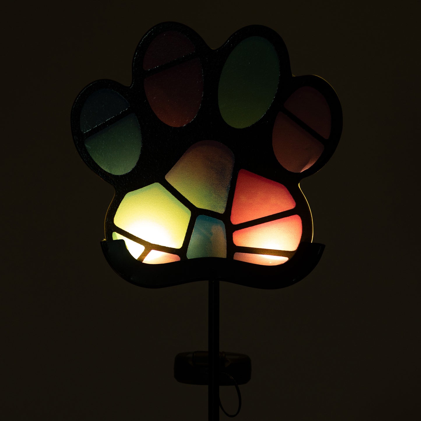 Colorful paw-shaped glowing garden stake on a black background