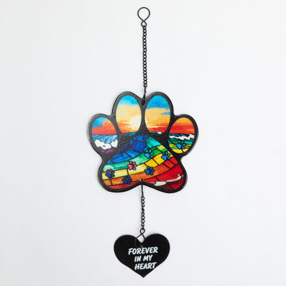 A hanging paw-shaped ornament with a colorful stained-glass-style sunset design and a black heart dangle that reads “FOREVER IN MY HEART,” shown against a plain light background.