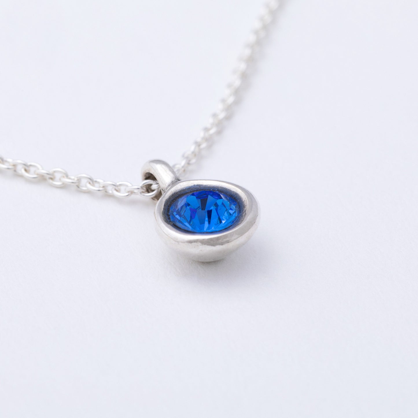 Silver necklace with a blue gemstone on a white background