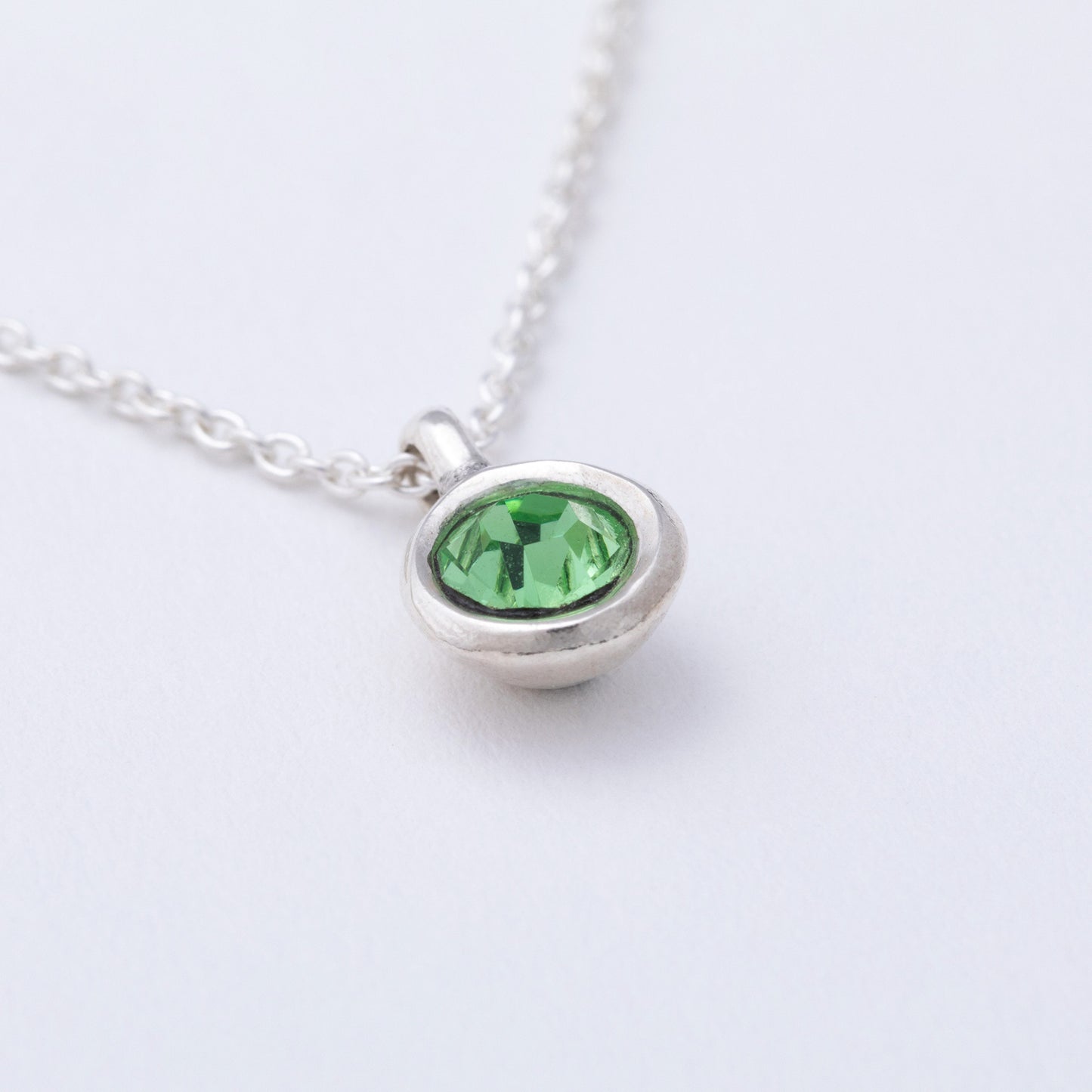 Silver necklace with a green gemstone pendant on a white background