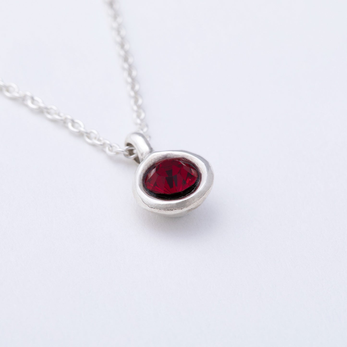 Silver necklace with a red gemstone pendant on a white background