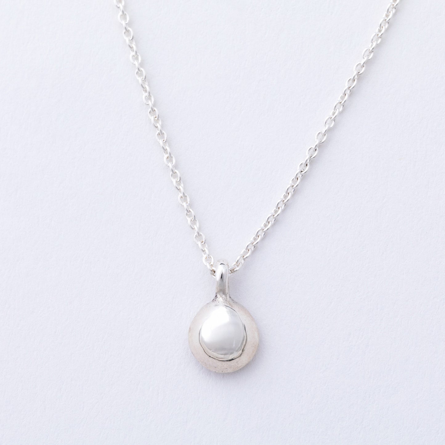 Silver necklace with a round pendant on a light gray background