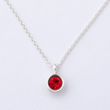 Silver necklace with a red gemstone pendant on a light gray background