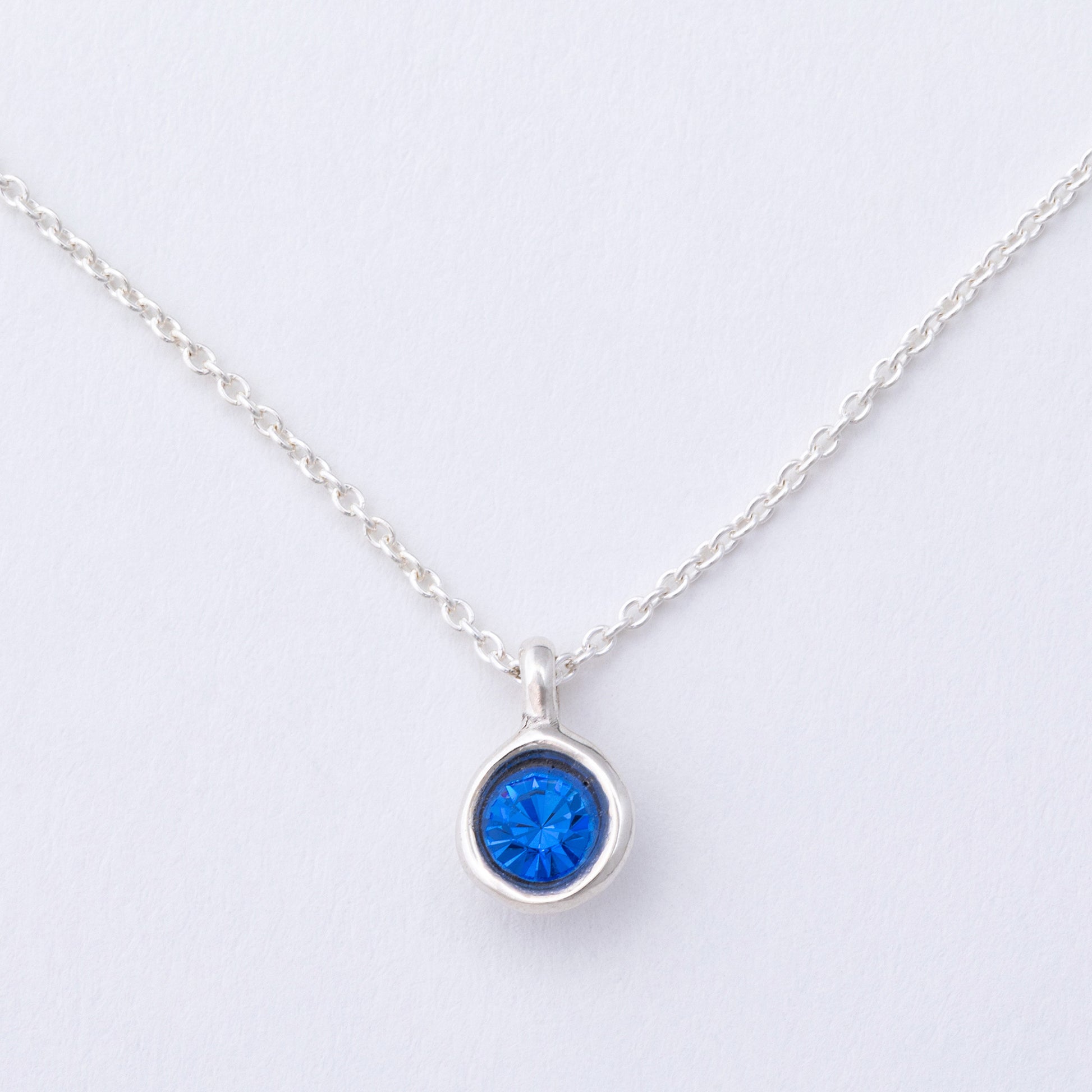 Silver necklace with a blue gemstone pendant on a light gray background