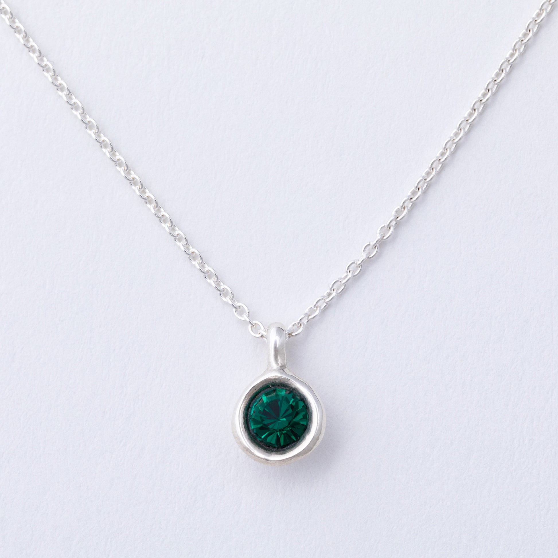 Silver necklace with a green gemstone pendant on a light gray background
