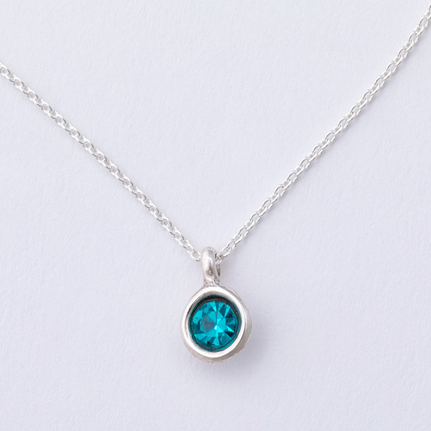 Silver necklace with a blue gemstone pendant on a light gray background
