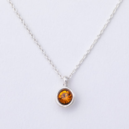 Silver necklace with a round amber-colored gemstone on a light gray background