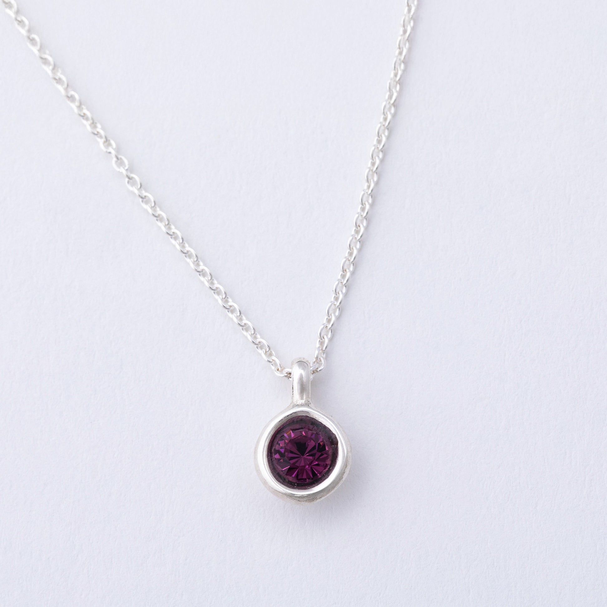 Silver necklace with a purple gemstone pendant on a light gray background
