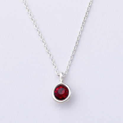 Silver necklace with a red gemstone pendant on a light gray background
