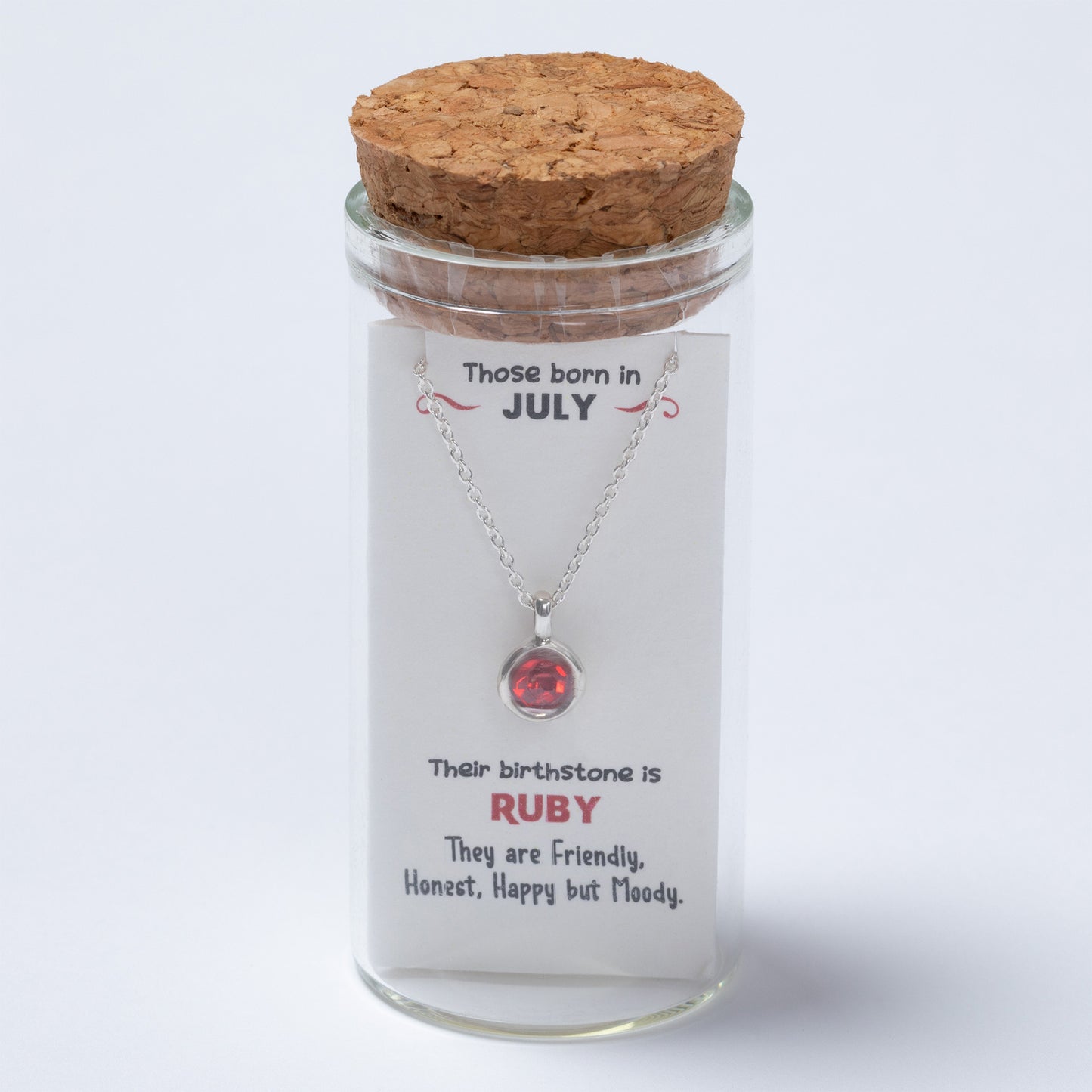 Necklace with a red gemstone in a glass jar with a cork lid, featuring text about July-born individuals and their birthstone.