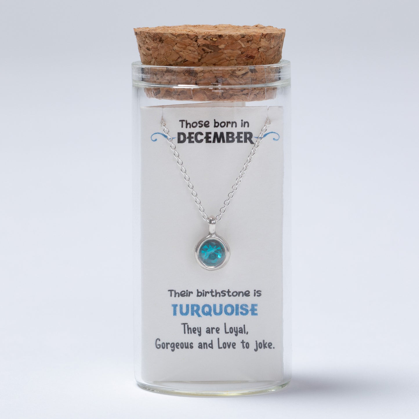 Necklace in a glass jar with a cork lid, featuring information about December-born individuals and their birthstone.