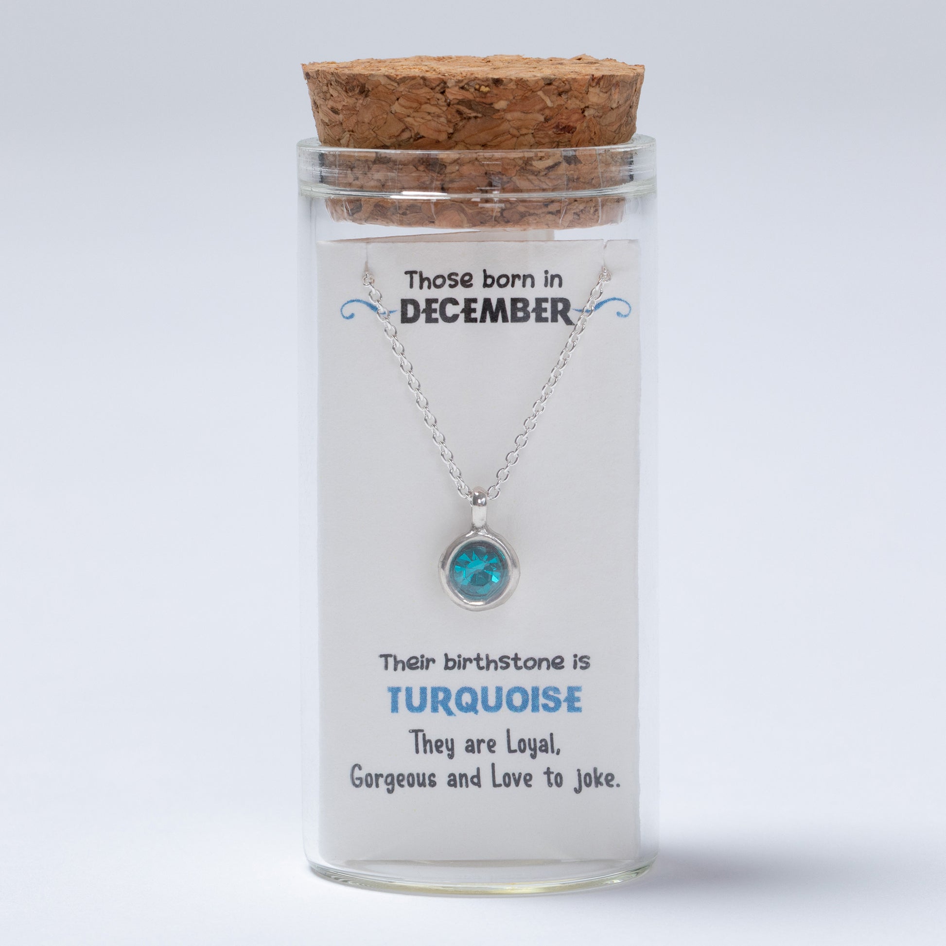 Necklace in a glass jar with a cork lid, featuring information about December-born individuals and their birthstone.