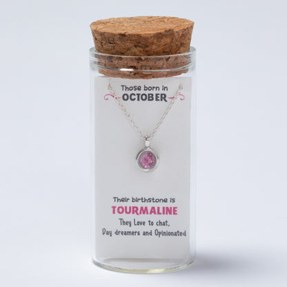 Glass jar with cork lid containing a necklace and a card about October-born individuals and their birthstone.
