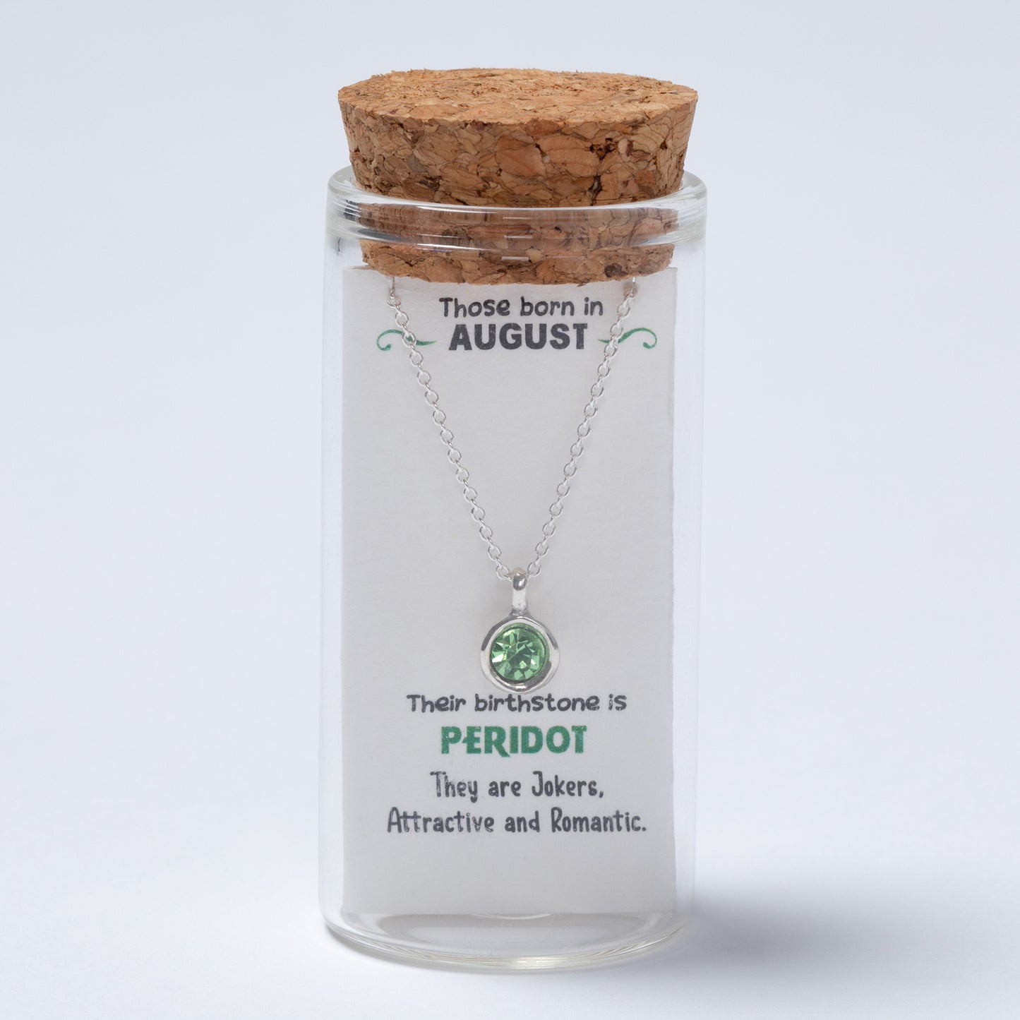 Glass jar with cork lid containing a necklace with a green gemstone, on a light gray background.